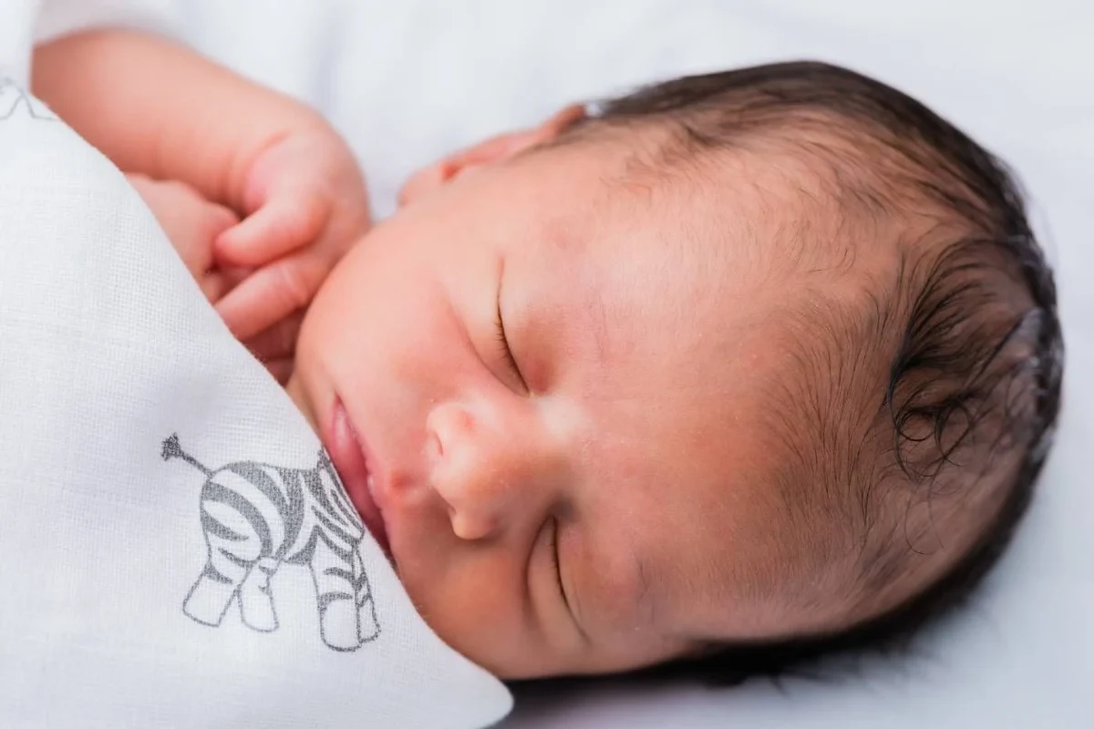 Newborn baby sleeping safely in a simple bassinet with feeding and diaper care essentials nearby
