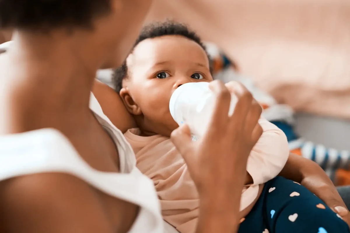 Newborn sleeping beside diaper log, feeding bottle, and soft blanket in a calm nursery